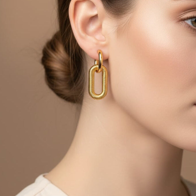 Close-up of a woman wearing gold hoop earrings against a beige background