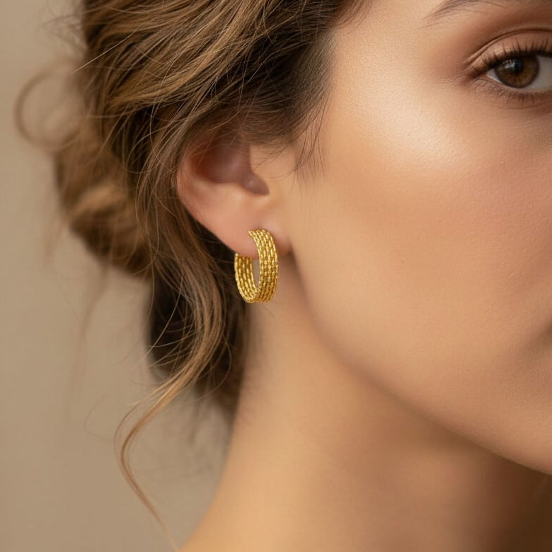 Close-up of a woman wearing gold hoop earrings with a neutral background