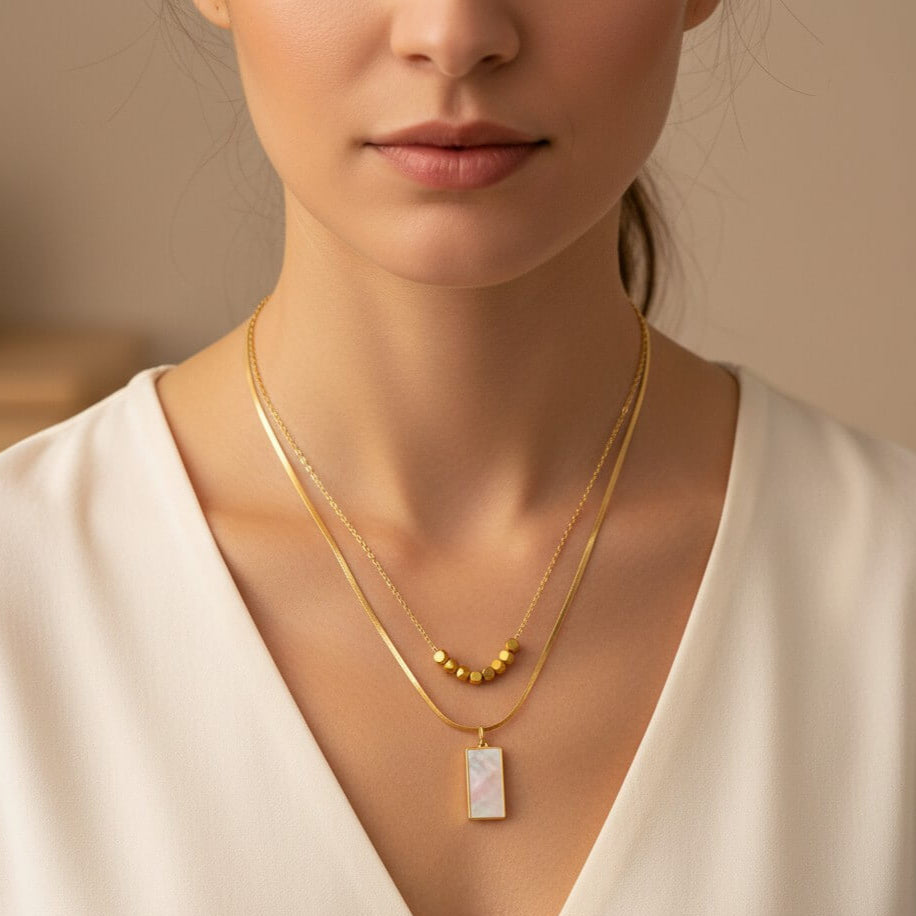 Woman wearing a gold necklace with a pendant against a neutral background